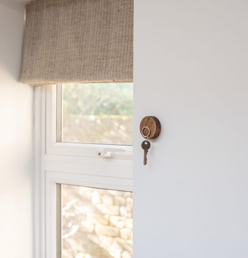 Peut inclure: Un porte-cl&eacute;s en bois avec un anneau m&eacute;tallique fix&eacute; &agrave; un mur blanc. Une cl&eacute; est accroch&eacute;e &agrave; l'anneau.