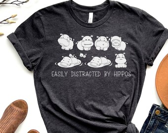 May include: Dark grey heather t-shirt with a white graphic of hippos in a pond and the text "Easily Distracted by Hippos".