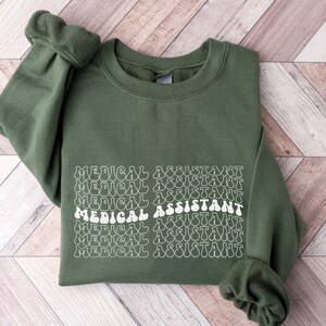 May include: A green sweatshirt with the text "MEDICAL ASSISTANT" repeated in a retro font style.