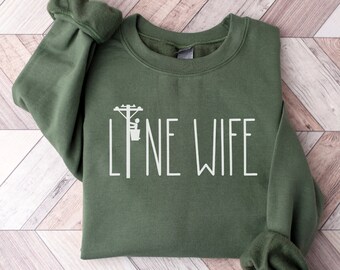 May include: A green sweatshirt with the text "LINE WIFE" in white lettering. A small graphic of a lineman on a utility pole is above the text.