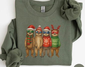 May include: Military green sweatshirt featuring a graphic of four sloths wearing sunglasses and holiday attire. One sloth wears a Santa hat and scarf, another a striped hat, a third a Santa hat and sweater, and the last a reindeer antler headband and sweater.