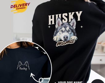 Op de afbeelding: Zwart sweatshirt met een husky-hond grafiek op de rug en de tekst "Husky mama". De voorkant van het sweatshirt heeft een witte omtrek van een husky-hond met de tekst "Rocky" eronder.