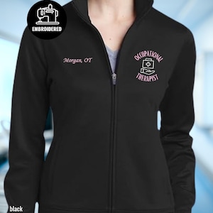 May include: Black zip-up jacket with the text "Occupational Therapist" and "Morgan, OT" in pink. A circular logo with a sewing machine and the word "Embroidered" is on the upper left. The word "black" is at the bottom.
