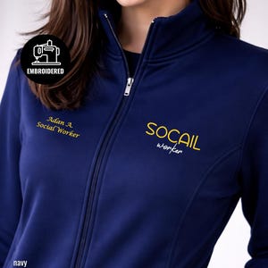 May include: Navy blue zip-up jacket with embroidered text. The jacket features the text "SOCAIL worker" in yellow and "Adan A. Social Worker" in yellow. The jacket has a high collar and a zipper closure. The word "navy" is at the bottom.