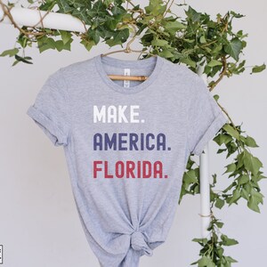 May include: Gray t-shirt with the text "MAKE. AMERICA. FLORIDA." in white, blue, and red lettering.