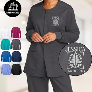 Może przedstawiać: Ciemnoszara kurtka medyczna z haftowanym z przodu napisem "JESSICA" i "RADIOLOGY". Kurtka ma okrągły dekolt, długie rękawy i dwie przednie kieszenie. Wyświetlany jest wybór koszul z długim rękawem w różnych kolorach.