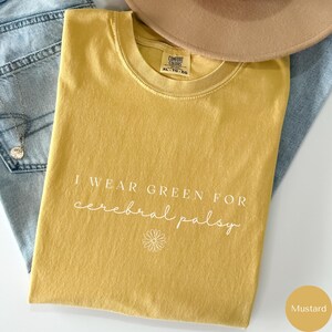 May include: Mustard yellow t-shirt with the text "I wear green for cerebral palsy" in white lettering. A small white daisy is below the text.