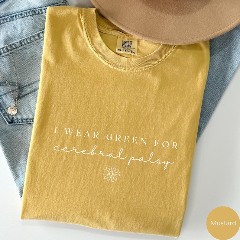 May include: Mustard yellow t-shirt with the text "I wear green for cerebral palsy" in white lettering. A small white daisy is below the text.