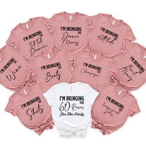 May include: A set of nine t-shirts with different sayings for a party. The shirts are in two colours: white and a light pink. The sayings on the shirts include "I'm bringing the wine", "I'm bringing the dance moves", "I'm bringing the fit not dancer", "I'm bringing the booty", "I'm bringing the attitude", "I'm bringing the champagne", "I'm bringing the bail money", "I'm bringing the shots", and "I'm bringing the 60 reasons for the party".