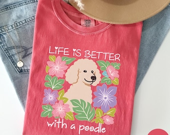 May include: A coral-colored t-shirt with the text "LIFE IS BETTER with a poodle" and a graphic of a poodle surrounded by flowers. The shirt is made of a soft material and is a comfortable fit.