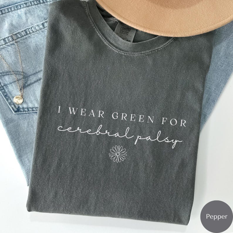 May include: A dark gray t-shirt with the text "I wear green for cerebral palsy" in white lettering. A small white daisy is below the text.