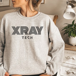 Może przedstawiać: Szara bluza z czarnym napisem "XRAY TECH" w paskowanym kroju.