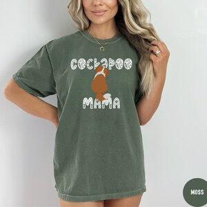May include: A green t-shirt with a white graphic of a brown and white Cockapoo dog with the text "Cockapoo Mama" in white.
