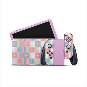 Puede incluir: Una consola Nintendo Switch lavanda y mandos con un estampado floral. Los mandos tienen agarres y botones negros. La funda de la consola presenta un diseño a juego con flores y rayas en colores pastel.