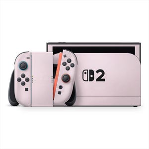 May include: A light pink Nintendo Switch console with matching Joy-Con controllers. The console features the Nintendo Switch logo and the number 2 in black. The Joy-Cons have black buttons and joysticks with blue and red accents.