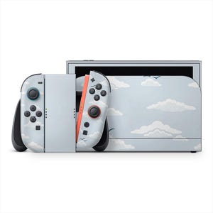 Könnte beinhalten: Eine Nintendo Switch-Konsole und Joy-Con-Controller mit einem hellblauen und weißen Wolkenmuster. Die Controller haben schwarze Knöpfe und Joysticks, einer mit orangefarbenen Akzenten. Auch die Dockingstation der Konsole hat das Wolkenmuster.