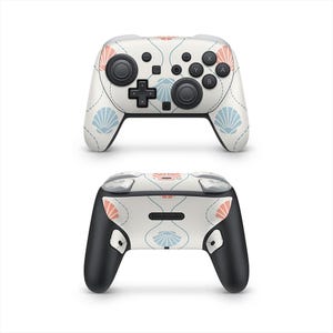 May include: A white Nintendo Switch Pro Controller featuring a floral and seashell design in coral and light blue. The controller has black joysticks and buttons, with the Nintendo logo on the back.