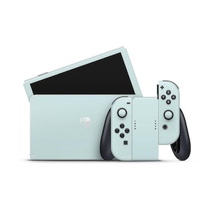 Könnte beinhalten: Minzfarbene Spielekonsole mit abnehmbaren Controllern. Die Konsole hat einen schwarzen Bildschirm und ein weißes Logo. Die Controller sind hellblau mit schwarzen Akzenten und Knöpfen. Für Handheld- oder Docking-Spielbetrieb.