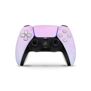 Könnte beinhalten: Ein rosa-weißer PlayStation 5 DualSense Wireless-Controller mit schwarzen Akzenten und Knöpfen. Der Controller hat eine strukturierte Oberfläche und ein PlayStation-Logo auf der Vorderseite.