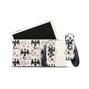 May include: A white gaming console with a matching case and controllers. The case and controllers feature a repeating pattern of black dragons, pink flowers, and swords on a white background. The console is designed for gaming.