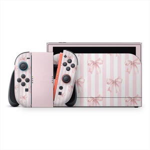 Może przedstawiać: Różowo-biała konsola Nintendo Switch z wzorem kokardek. Kontrolery Joy-Con i sama konsola mają wzór różowych kokardek na paskowanym tle. Przyciski i joysticki są czarne i niebieskie.