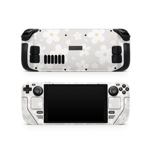 May include: A white handheld gaming console with a floral pattern featuring white and yellow flowers. The console has black accents on the sides and buttons. The screen is black and the console is shown from two angles.