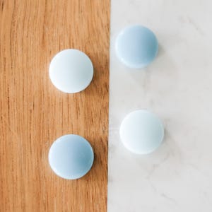 May include: Four round, light blue and white glass decorative objects. Two are light blue and two are white. The objects are arranged on a wooden surface and a white marble surface.