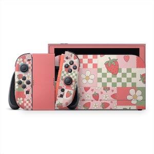 Może przedstawiać: Różowa konsola Nintendo Switch z pasującymi Joy-Conami. Konsola i kontrolery mają wzór patchworkowy z truskawkami, kwiatami i szachownicą. Przyciski i joysticki są czarne.