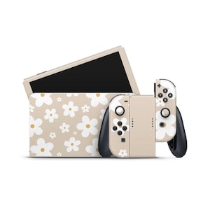 May include: A beige Nintendo Switch console and controllers with a white daisy floral pattern. The Switch screen is visible behind the console. The controllers have black accents and buttons.