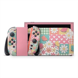 Puede incluir: Una consola Nintendo Switch rosa con mandos Joy-Con a juego. Los mandos y la consola presentan un diseño floral y de mariposas con colores pastel. El diseño incluye margaritas, mariposas, corazones y patrones de cuadros vichy.