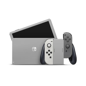Op de afbeelding: Een grijze Nintendo Switch-console met twee afneembare Joy-Con-controllers. Eén Joy-Con is wit en grijs, de andere is grijs. De console heeft een zwart scherm en een standaard. De controllers hebben knoppen en joysticks.