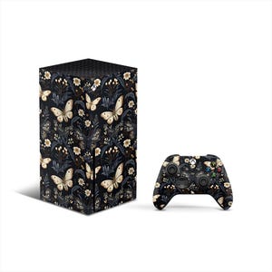 Könnte beinhalten: Eine schwarze Xbox Series X Konsole und ein Controller mit einem floralen Muster mit Schmetterlingen und Blättern. Das Muster ist in Gold-, Weiß- und Schwarztönen gehalten.
