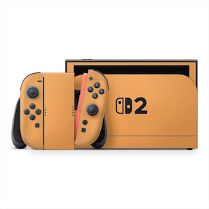 May include: A mustard-colored Nintendo Switch console with matching Joy-Con controllers. The console features black buttons and the text "Switch 2" printed on the front. The Joy-Cons have black and red accents.