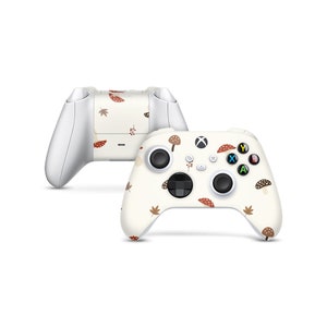 Könnte beinhalten: Ein weißer Xbox-Controller mit einer cremefarbenen Haut, die mit einem Muster aus braunen Pilzen und Blättern verziert ist. Der Controller verfügt über die Standard-Xbox-Tasten: A, B, X, Y und ein Richtungskreuz.