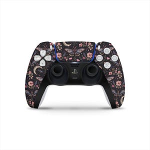 May include: A black and white PlayStation 5 controller with a floral and butterfly design. The controller has a black and white color scheme with a floral and butterfly design. The controller has a black and white color scheme with a floral and butterfly design.