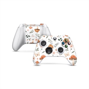 Könnte beinhalten: Zwei weiße Gamecontroller mit einem Blumen- und Pilzdesign. Die Controller weisen ein Muster aus orangefarbenen Pilzen, rosa Blumen und Schmetterlingen auf weißem Hintergrund auf. Die Knöpfe und Joysticks sind schwarz.