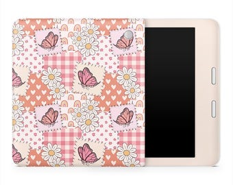 May include: A cream-colored e-reader with a patterned cover. The cover features a patchwork design with pink butterflies, white daisies, and small rainbows on a peach and pink background. The e-reader has a black screen and two buttons on the side.