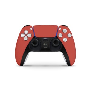 Puede incluir: Un mando inalámbrico PlayStation 5 DualSense rojo y negro con botones blancos y el logotipo de PlayStation.
