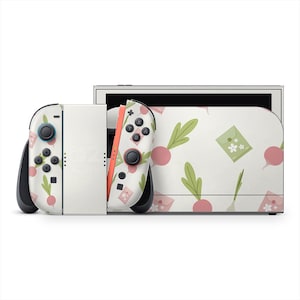 May include: A white Nintendo Switch console with a custom skin featuring a pattern of pink radishes, green leaves, and small green envelopes. The Joy-Con controllers have the same design. The console is set against a white background.