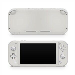 Könnte beinhalten: Eine weiße Handheld-Spielkonsole, von vorne und hinten gezeigt. Die Vorderansicht zeigt einen schwarzen Bildschirm, Steuertasten und ein Steuerkreuz. Die Rückansicht zeigt eine glatte Oberfläche mit Lüftungsschlitzen und Anschlüssen. Die Konsole hat eine helle, neutrale Farbe.