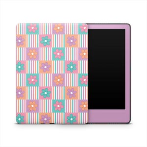 Op de afbeelding: Een lila e-reader met een kleurrijke hoes. De hoes heeft een patchwork-ontwerp met vierkanten van roze, turquoise, oranje en paarse bloemen. De vierkanten staan tegen een achtergrond van verticale strepen in bijpassende kleuren.