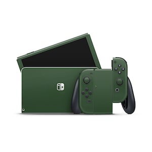 May include: A dark green Nintendo Switch console with matching Joy-Con controllers. The console is closed and the screen is off. The Joy-Cons are detached from the console and are lying on a white surface.
