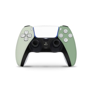 Peut inclure: Une manette sans fil DualSense PlayStation 5 blanche et verte avec des accents noirs. La manette a un logo PlayStation sur le devant et des boutons pour PlayStation, partager, options et pavé tactile.
