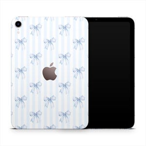Puede incluir: Un iPad de Apple con una funda decorativa con un patrón de lazos azul claro sobre un fondo a rayas blancas y azul claro. El logotipo de Apple es visible en la parte posterior del dispositivo.