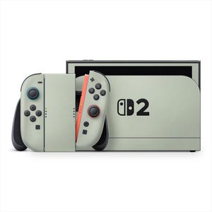 May include: A light green Nintendo Switch console and Joy-Con controllers. The controllers have black buttons and joysticks, with one controller featuring a coral-coloured side. The console's dock displays the Nintendo logo and the number 2.