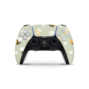 Könnte beinhalten: Ein grüner, weißer und gelber PlayStation 5 DualSense-Controller mit einem Bienen- und Honigtopf-Design. Der Controller hat eine schwarze Vorderseite mit zwei schwarzen Knöpfen.