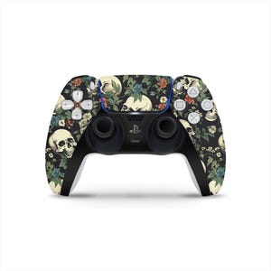 Puede incluir: Un mando de PlayStation 5 negro con un diseño floral y de calaveras. El mando tiene un esquema de color negro y blanco con un patrón floral y calaveras en todo el diseño.