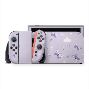 Op de afbeelding: Een lavendelkleurige Nintendo Switch-console met bijpassende Joy-Con-controllers. De console en controllers hebben een herhaald patroon van paarse vlinders, witte bloemen en een wolk met regendruppels.