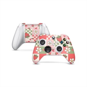 May include: Two white and pink game controllers. The front controller has a pink, green, and white strawberry and flower pattern. The back controller has a matching design on the top. The buttons are black, and the letters are green, yellow, blue, and red.