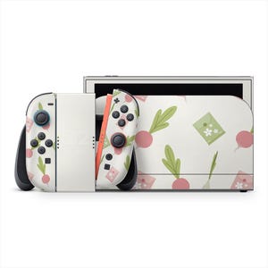 May include: A white Nintendo Switch console with a custom skin featuring a pattern of pink radishes, green leaves, and small floral envelopes. The Joy-Con controllers have black buttons and joysticks. The console is set against a white background.